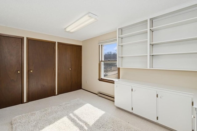 unfurnished bedroom featuring light colored carpet, two closets, and a baseboard heating unit