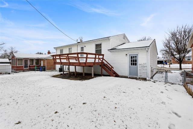 snow covered house with a deck, a gate, fence, stairway, and a sunroom