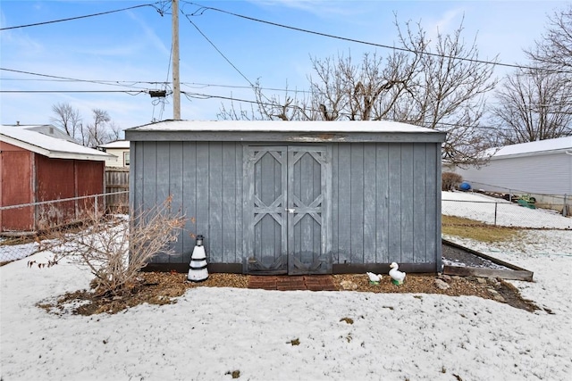 snow covered structure featuring an outbuilding, a storage unit, and fence