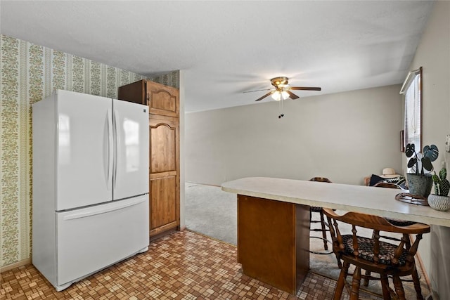 kitchen featuring brown cabinets, a kitchen breakfast bar, freestanding refrigerator, a peninsula, and light countertops