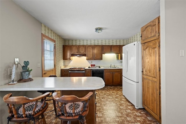 kitchen featuring a sink, freestanding refrigerator, a peninsula, wallpapered walls, and stove