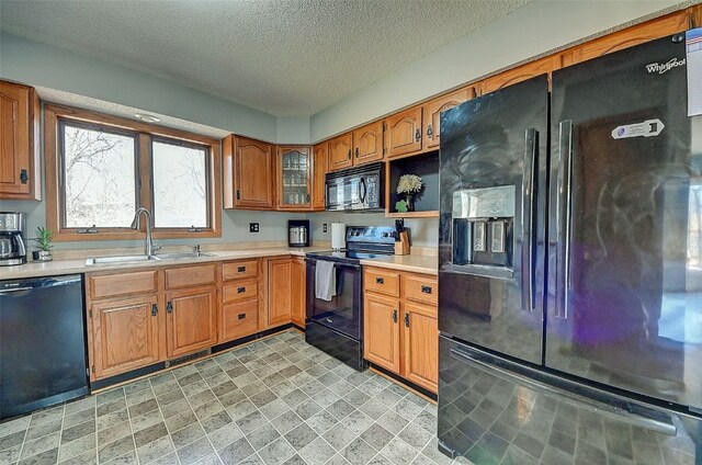 kitchen featuring brown cabinets, black appliances, a sink, a textured ceiling, and light countertops