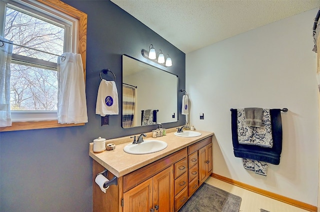 bathroom with a sink, baseboards, a textured ceiling, and double vanity