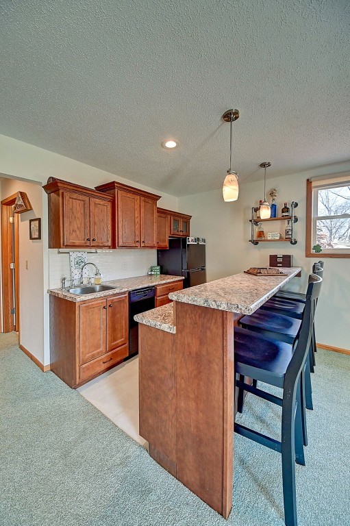 kitchen with light colored carpet, light countertops, brown cabinets, black appliances, and a sink