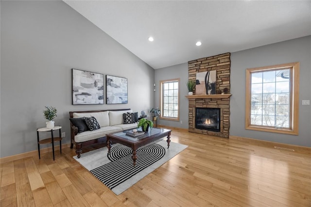 living room featuring light wood-style flooring, a fireplace, high vaulted ceiling, and baseboards