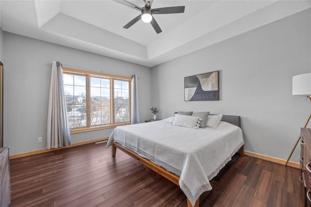 bedroom with baseboards, a raised ceiling, wood finished floors, and a ceiling fan