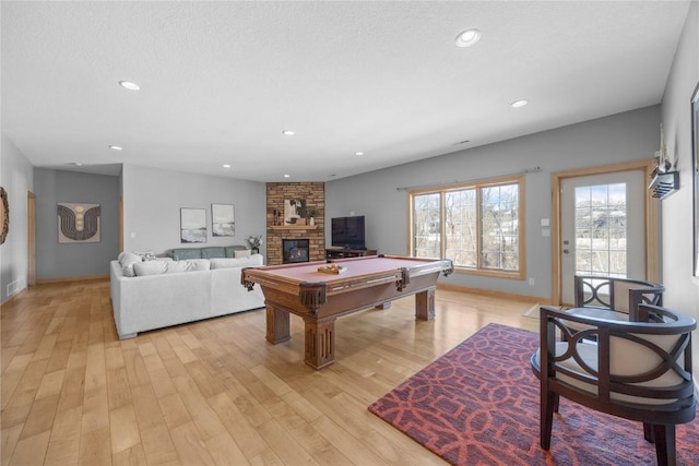 recreation room with recessed lighting, a stone fireplace, and light wood finished floors