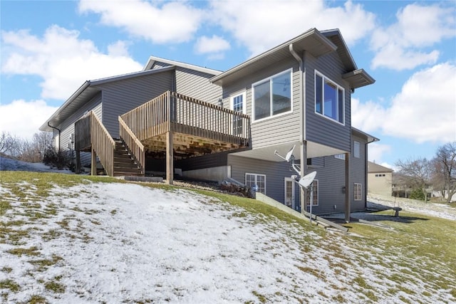 snow covered rear of property with a wooden deck and stairs