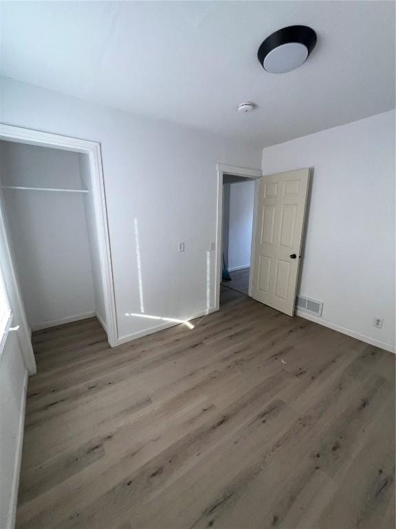 unfurnished bedroom with visible vents, baseboards, a closet, and wood finished floors