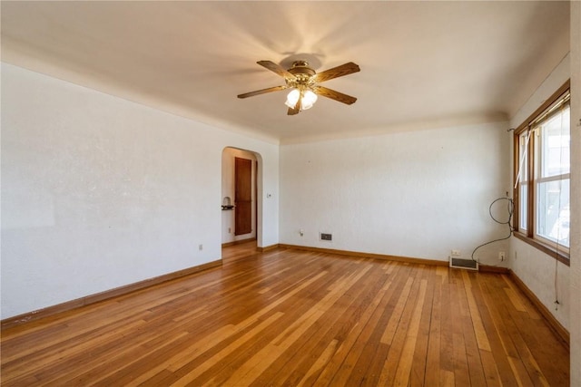 unfurnished room with visible vents, a ceiling fan, arched walkways, light wood-style floors, and baseboards