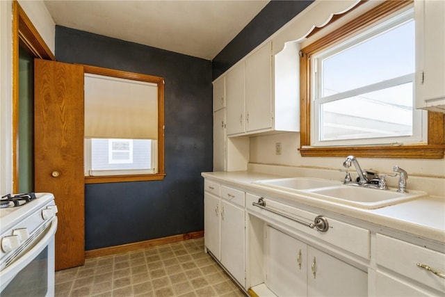 kitchen with light countertops, white cabinets, white gas range oven, and a sink