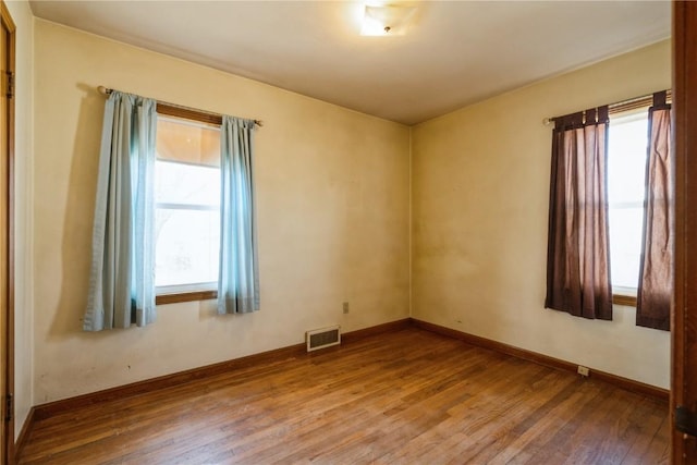 empty room featuring visible vents, baseboards, and hardwood / wood-style flooring