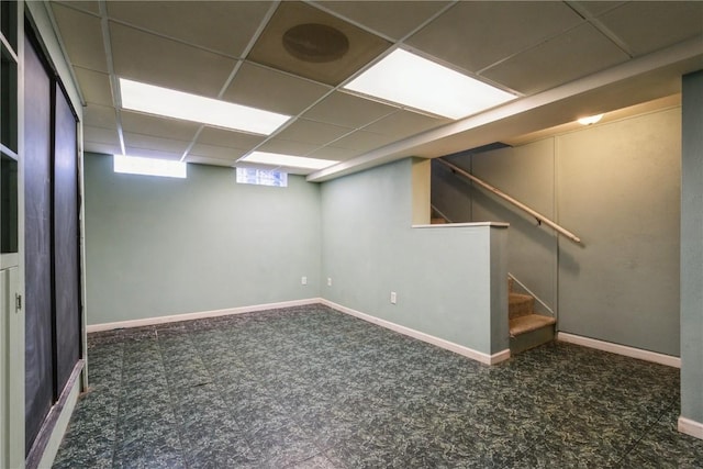 below grade area featuring baseboards, a paneled ceiling, carpet floors, and stairs