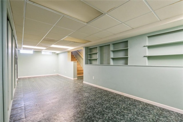 basement with tile patterned floors, stairway, baseboards, and a drop ceiling