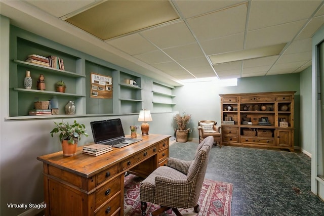 home office with built in features, a paneled ceiling, carpet floors, and baseboards