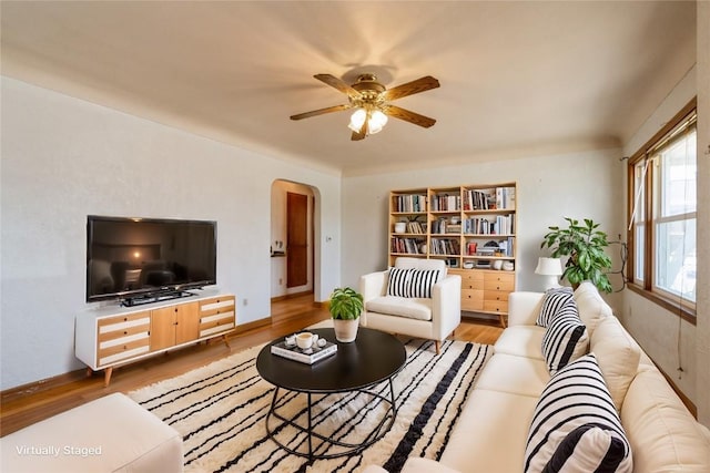 living room featuring a ceiling fan, wood finished floors, arched walkways, and baseboards