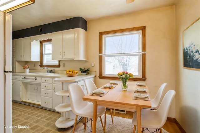 kitchen with light countertops, white cabinets, baseboards, and a sink