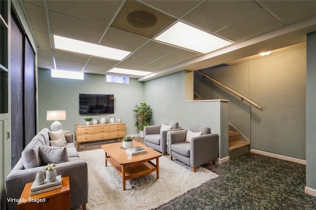 living room featuring stairway, baseboards, and a drop ceiling