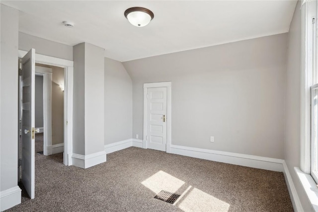 carpeted empty room featuring baseboards and vaulted ceiling