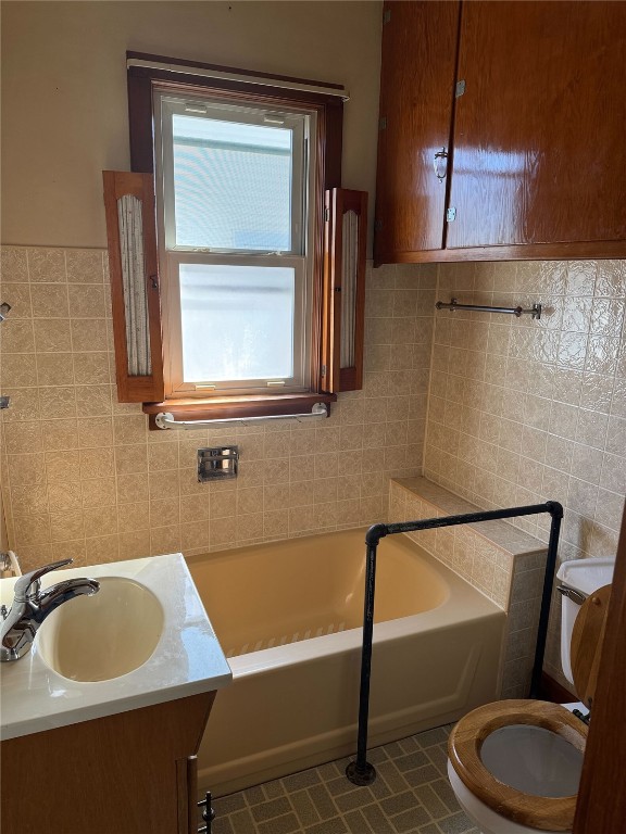 bathroom with toilet, tile walls, a bath, and vanity