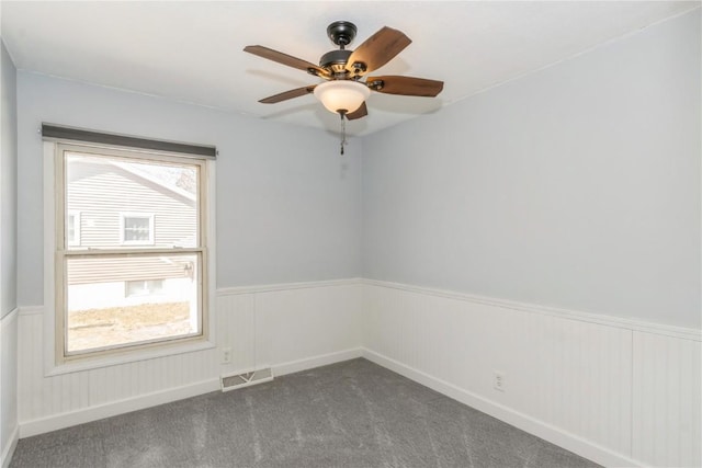 carpeted spare room with visible vents, a wainscoted wall, and a ceiling fan