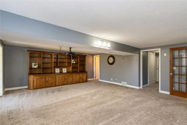 unfurnished living room with light carpet, visible vents, a textured ceiling, and baseboards