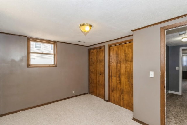 unfurnished bedroom featuring two closets, baseboards, carpet, and crown molding