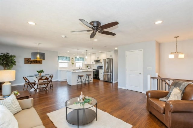 living area featuring ceiling fan with notable chandelier, recessed lighting, dark wood-style flooring, and baseboards