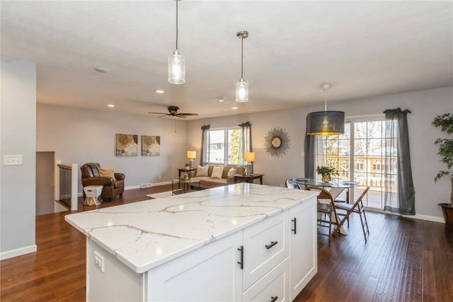 kitchen with light stone countertops, dark wood finished floors, a center island, and white cabinets