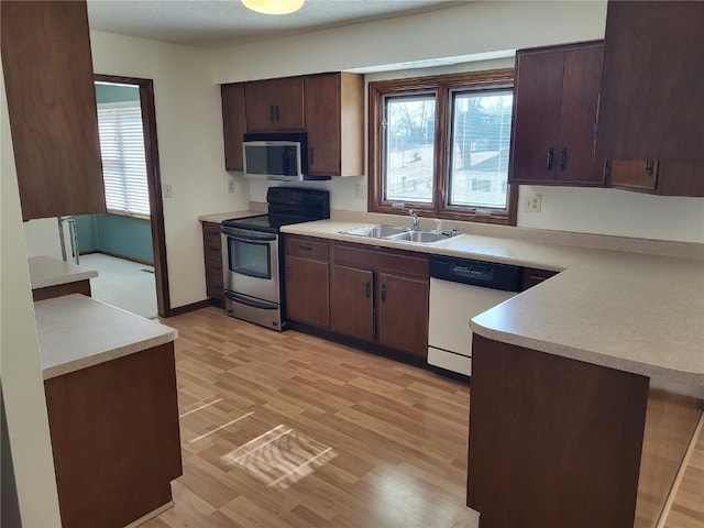 kitchen featuring light wood finished floors, a sink, light countertops, dark brown cabinets, and appliances with stainless steel finishes