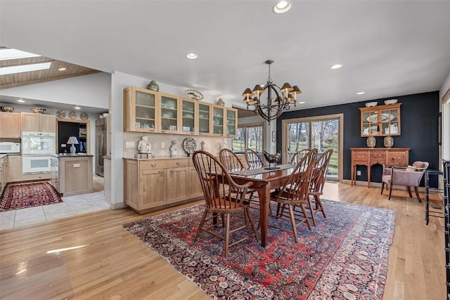 dining room featuring lofted ceiling with skylight, recessed lighting, light wood-style floors, and an inviting chandelier