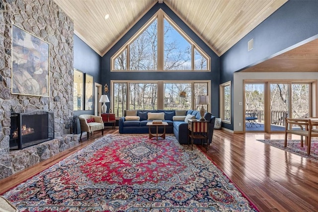 living area with hardwood / wood-style floors, baseboards, high vaulted ceiling, a stone fireplace, and wooden ceiling