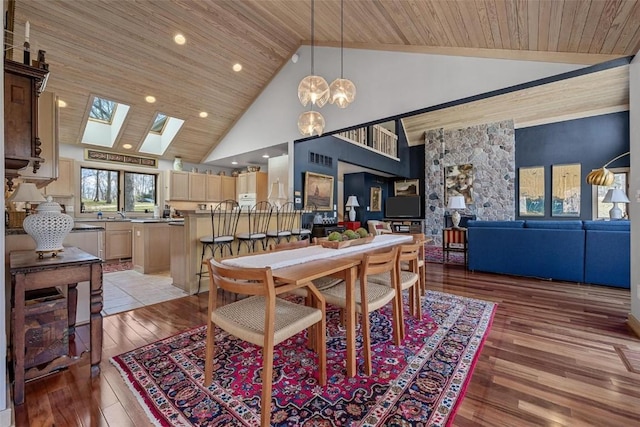 dining area featuring a skylight, high vaulted ceiling, light wood finished floors, and wood ceiling