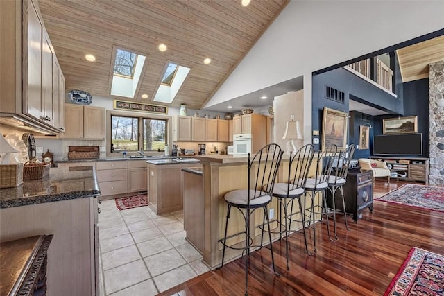 kitchen featuring visible vents, white oven, a skylight, light brown cabinetry, and wooden ceiling