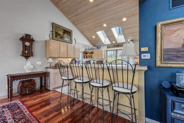 kitchen featuring a kitchen bar, light brown cabinetry, wood finished floors, wooden ceiling, and a skylight