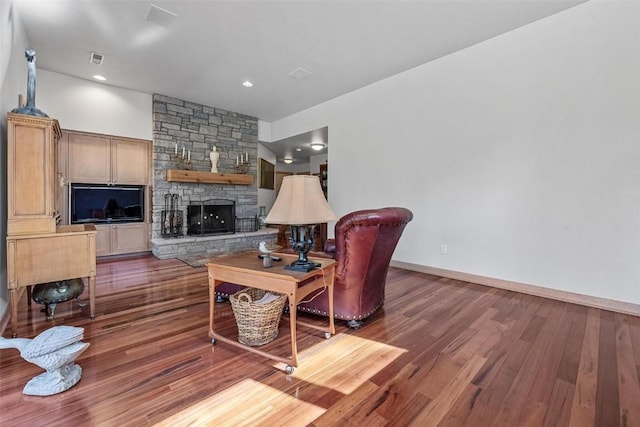 living area featuring a stone fireplace, baseboards, visible vents, and wood finished floors