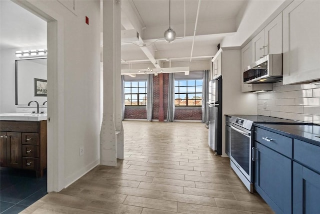 kitchen with beamed ceiling, a sink, wood finished floors, appliances with stainless steel finishes, and decorative backsplash