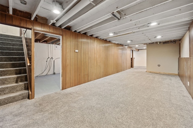 finished basement featuring carpet flooring, wooden walls, and stairs