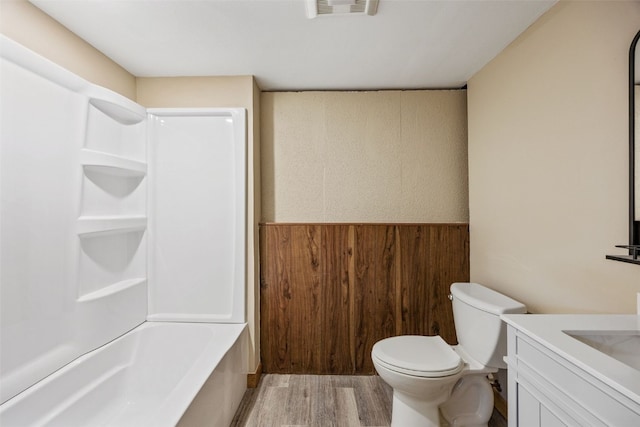 bathroom featuring wooden walls, wood finished floors, visible vents, a wainscoted wall, and toilet