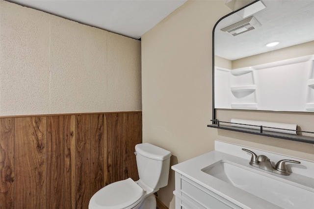 bathroom with visible vents, a wainscoted wall, toilet, wood walls, and vanity