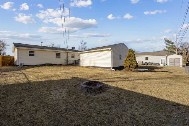 back of house featuring a fire pit, an outdoor structure, a lawn, and fence