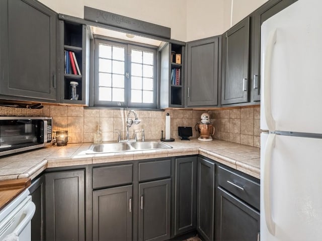 kitchen featuring open shelves, freestanding refrigerator, a sink, decorative backsplash, and stainless steel microwave