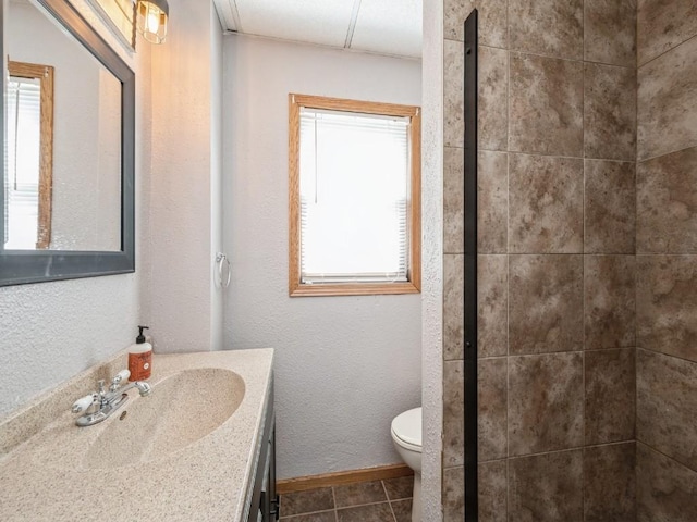 full bath featuring toilet, tiled shower, tile patterned flooring, baseboards, and vanity