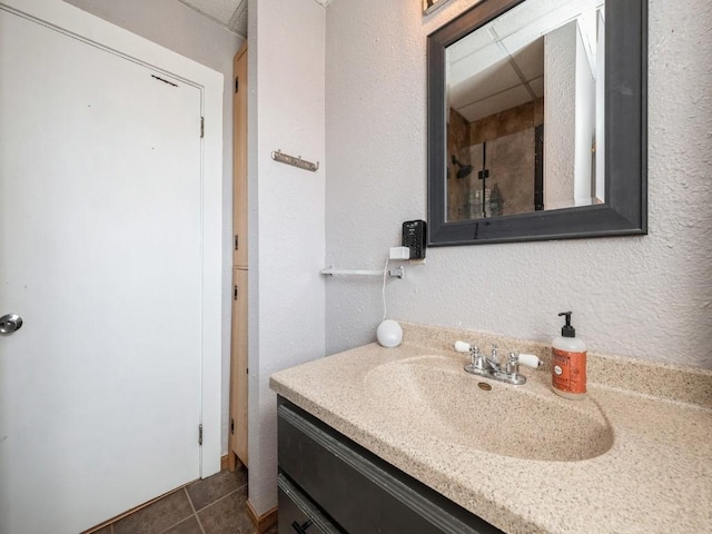 bathroom with a textured wall, a drop ceiling, vanity, and tile patterned flooring