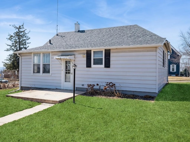 rear view of property with a patio area, a lawn, a chimney, and roof with shingles