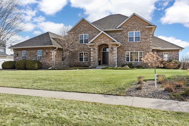 view of front facade with brick siding, a shingled roof, and a front lawn