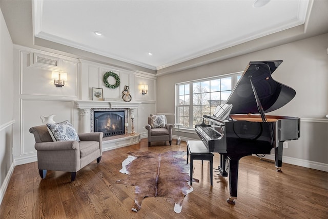 living area with wood finished floors, a fireplace, a raised ceiling, and ornamental molding