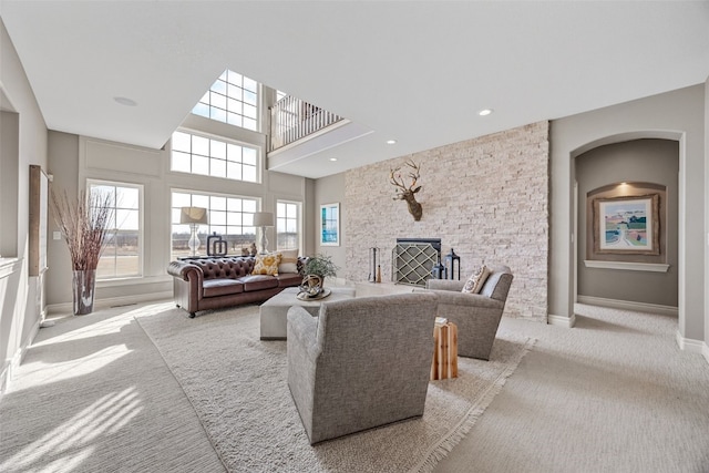 carpeted living area featuring a stone fireplace, a high ceiling, recessed lighting, and baseboards