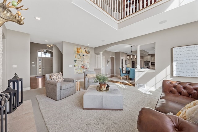 living area featuring recessed lighting, arched walkways, decorative columns, baseboards, and a towering ceiling