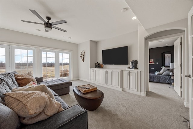 living room with a ceiling fan, baseboards, arched walkways, and light carpet